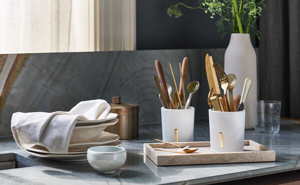Rituals candle jars repurposed for storing cutlery on a kitchen counter with natural light and neutral tones.
